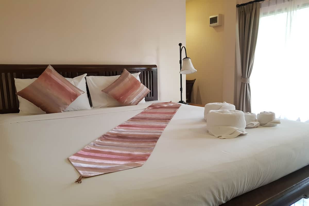 Una cama bien hecha con una toalla a rayas, almohadas y toallas enrolladas sobre un edredón blanco.