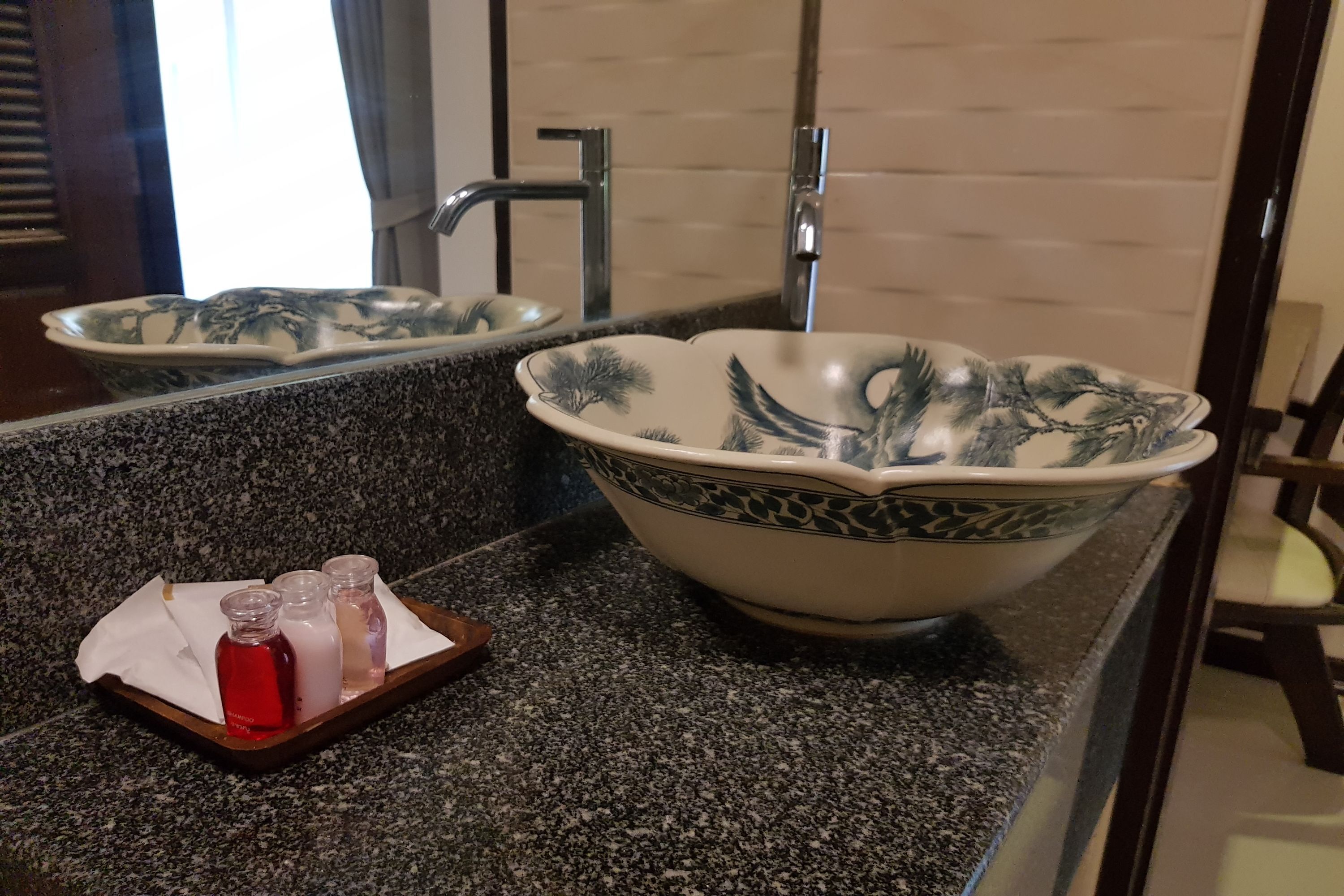 A bathroom with a granite countertop, a large bowl sink with a decorative pattern, and a mirror reflecting the sink and window.
