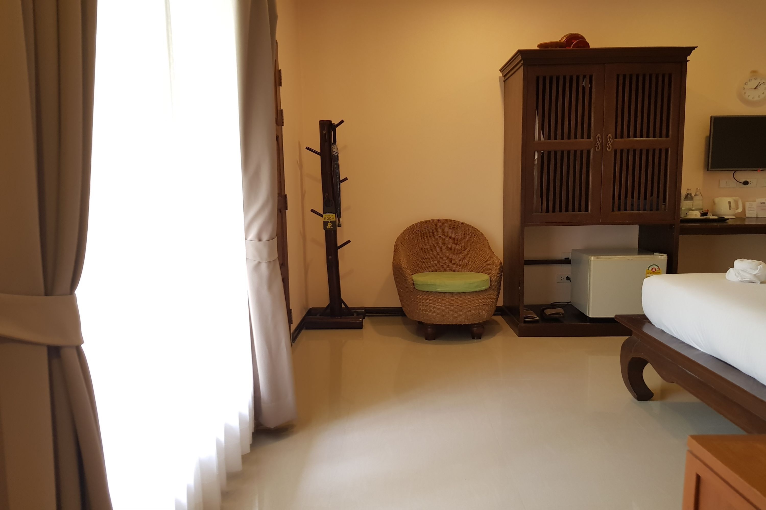 A hotel room with a bed, a wooden wardrobe, a wicker chair, a small table, and a television.