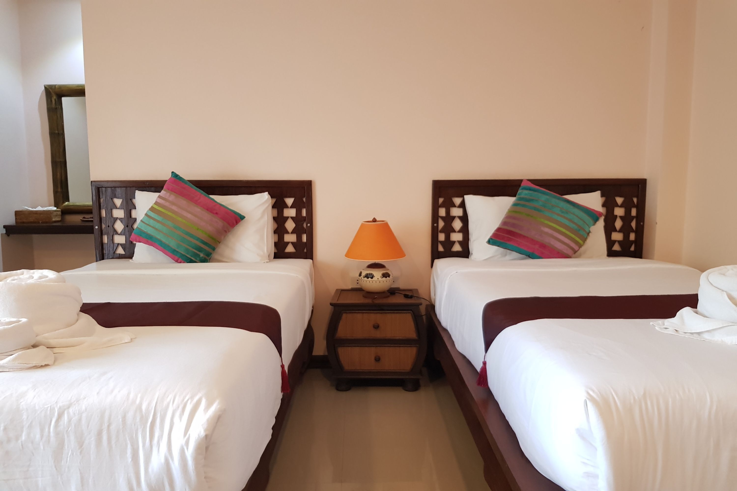 Een hotelkamer met twee bedden, elk voorzien van een kussen en een nachtkastje met een lamp.