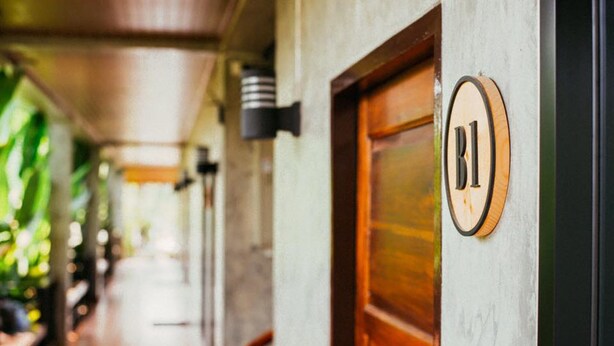 A corridor with a wooden door marked "B1" and a wall-mounted light fixture. - Pai Sukhothai Resort (Sukhothai)