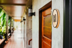 A corridor with a wooden door marked "B1" and a wall-mounted light fixture. - Pai Sukhothai Resort (Sukhothai)