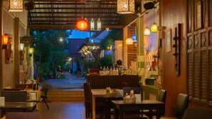 An indoor dining area with tables and chairs, a counter with food items, and hanging lanterns. - Pai Sukhothai Resort (Sukhothai)