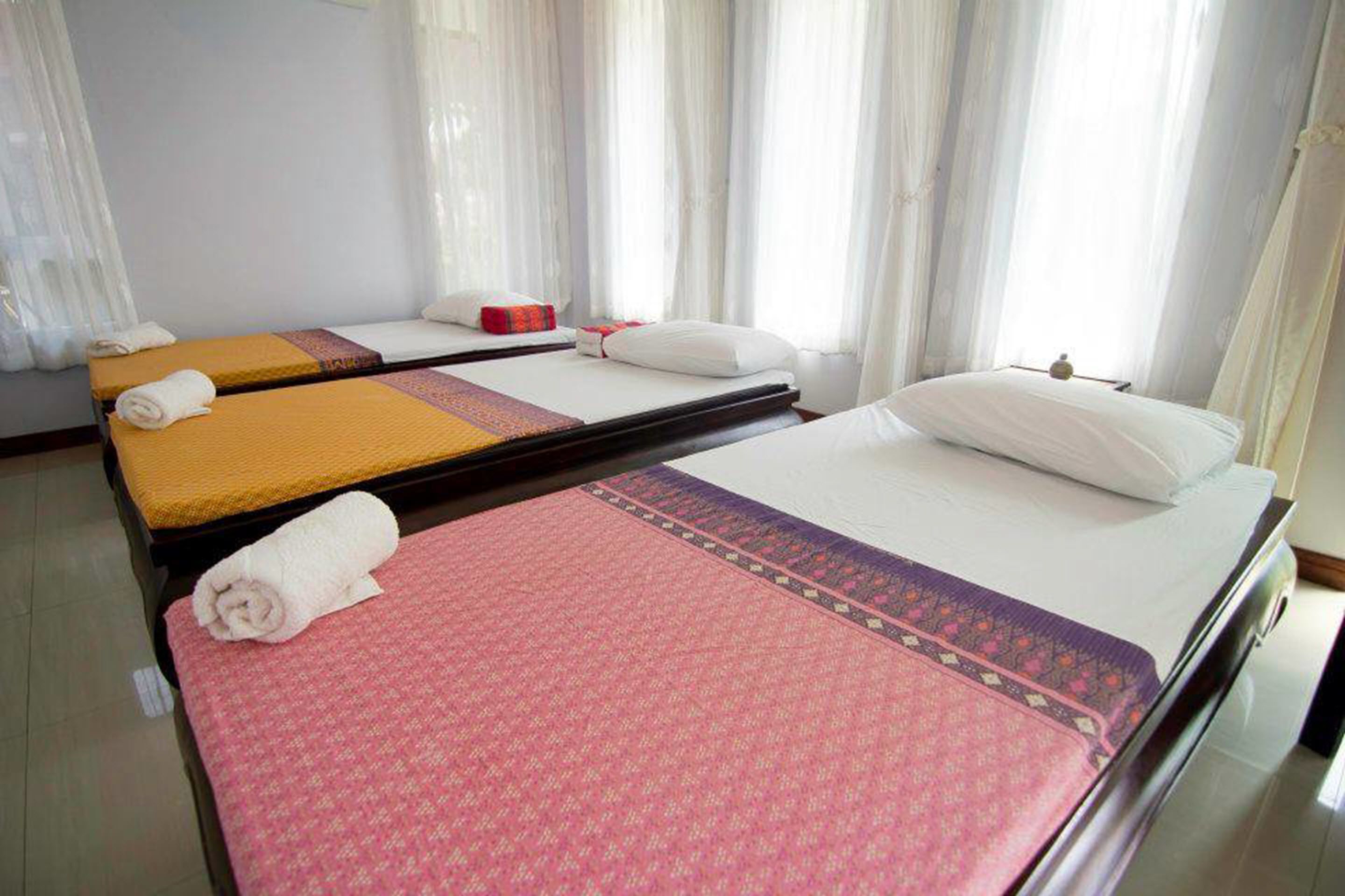 A hotel room with two single beds, each with a different colored bedspread and a rolled towel on the bed.