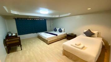 Una habitación de hotel con una cama grande, una cama más pequeña, un banco de madera, una mesita de noche y una ventana con cortinas.