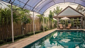 An indoor swimming pool with a glass ceiling, surrounded by bamboo fences and tropical plants. - Pai Sukhothai Resort (Sukhothai)