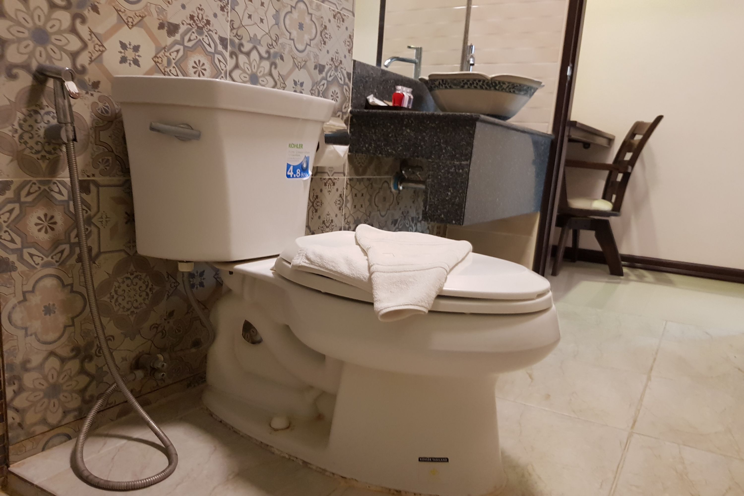 Un inodoro con tanque y tapa blancos, un dispensador de papel higiénico visible y una toalla sobre la tapa.