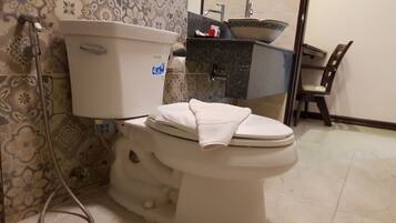 A toilet with a white tank and lid, a visible toilet paper holder, and a towel on the lid.