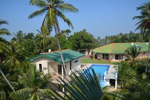 A resort with a swimming pool, palm trees, and a green-roofed building. - Hilltop Boosa (Boossa)