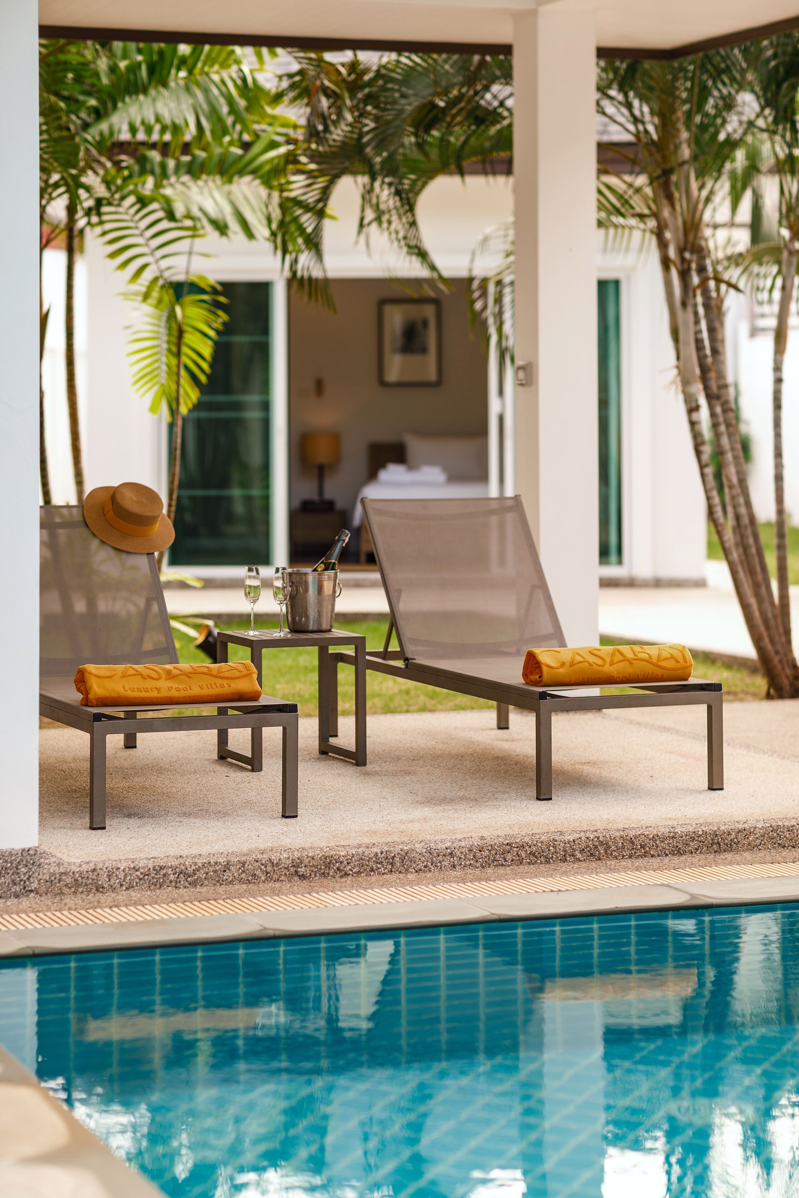 A poolside area with lounge chairs, a bucket with a bottle, and a hat on one of the chairs.