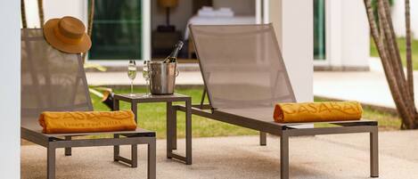 A poolside area with lounge chairs, a bucket with a bottle, and a hat on one of the chairs.
