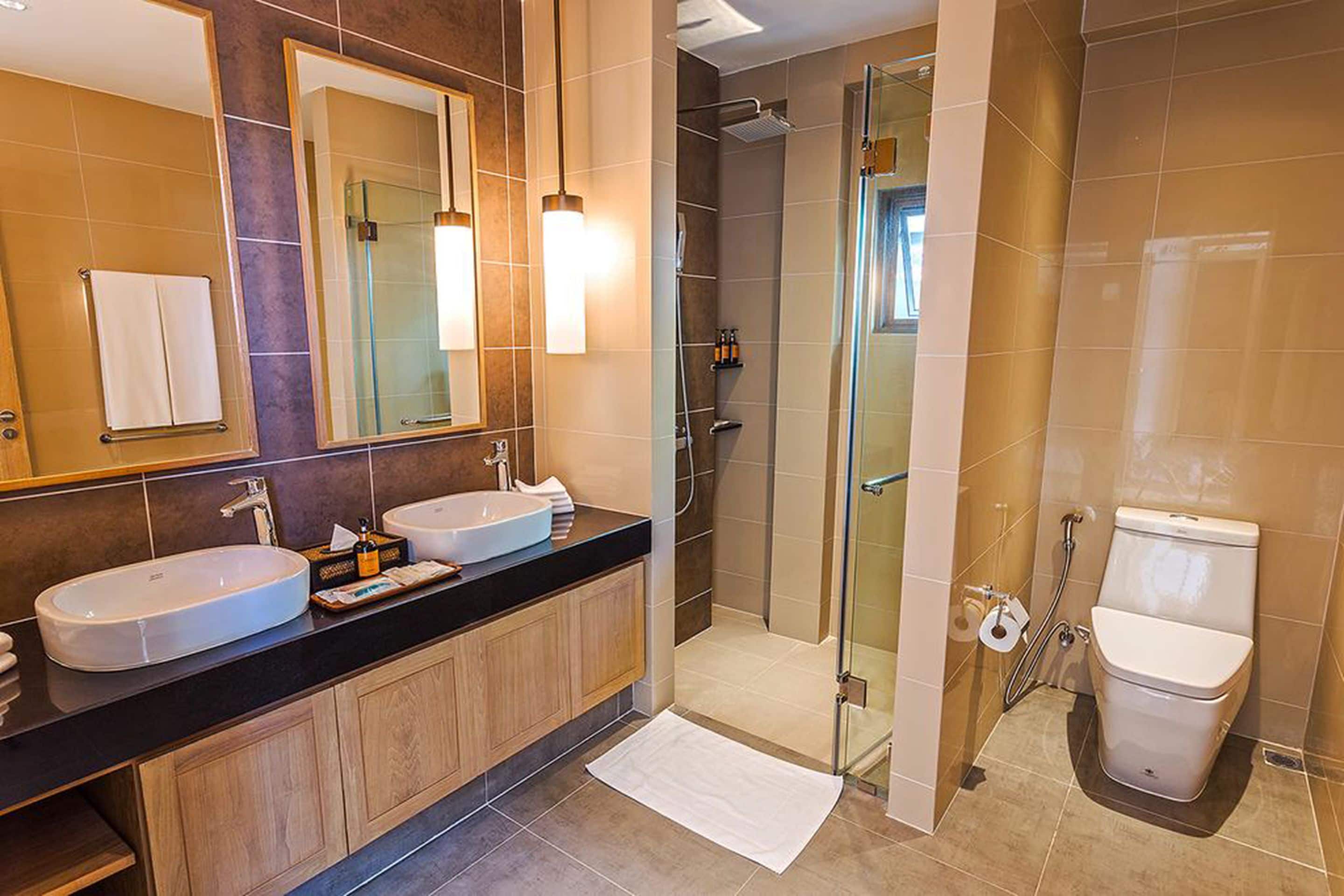 A modern bathroom with two sinks, a glass shower enclosure, and a toilet.