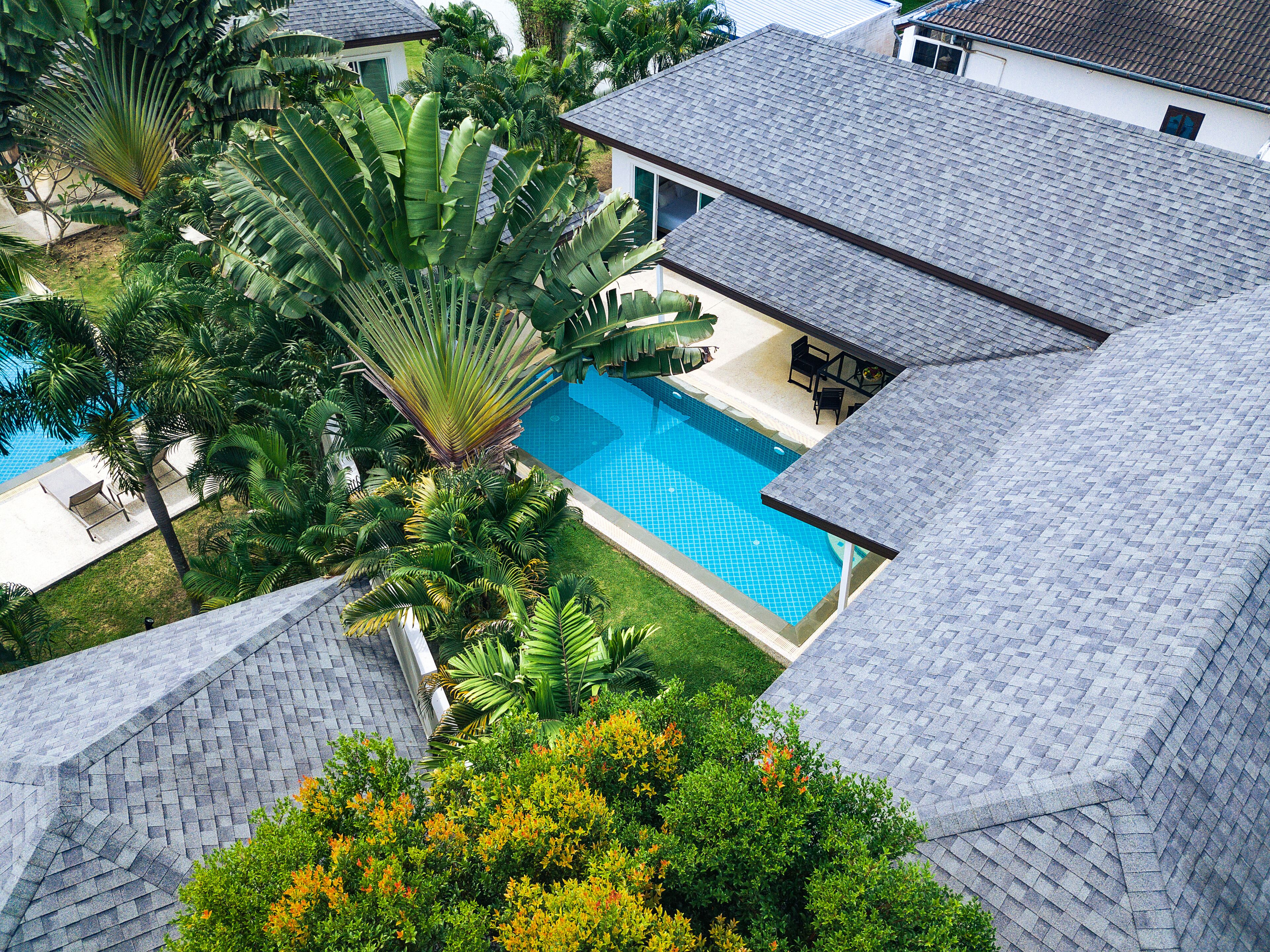 A residential area with a swimming pool surrounded by lush greenery and a tiled roof.