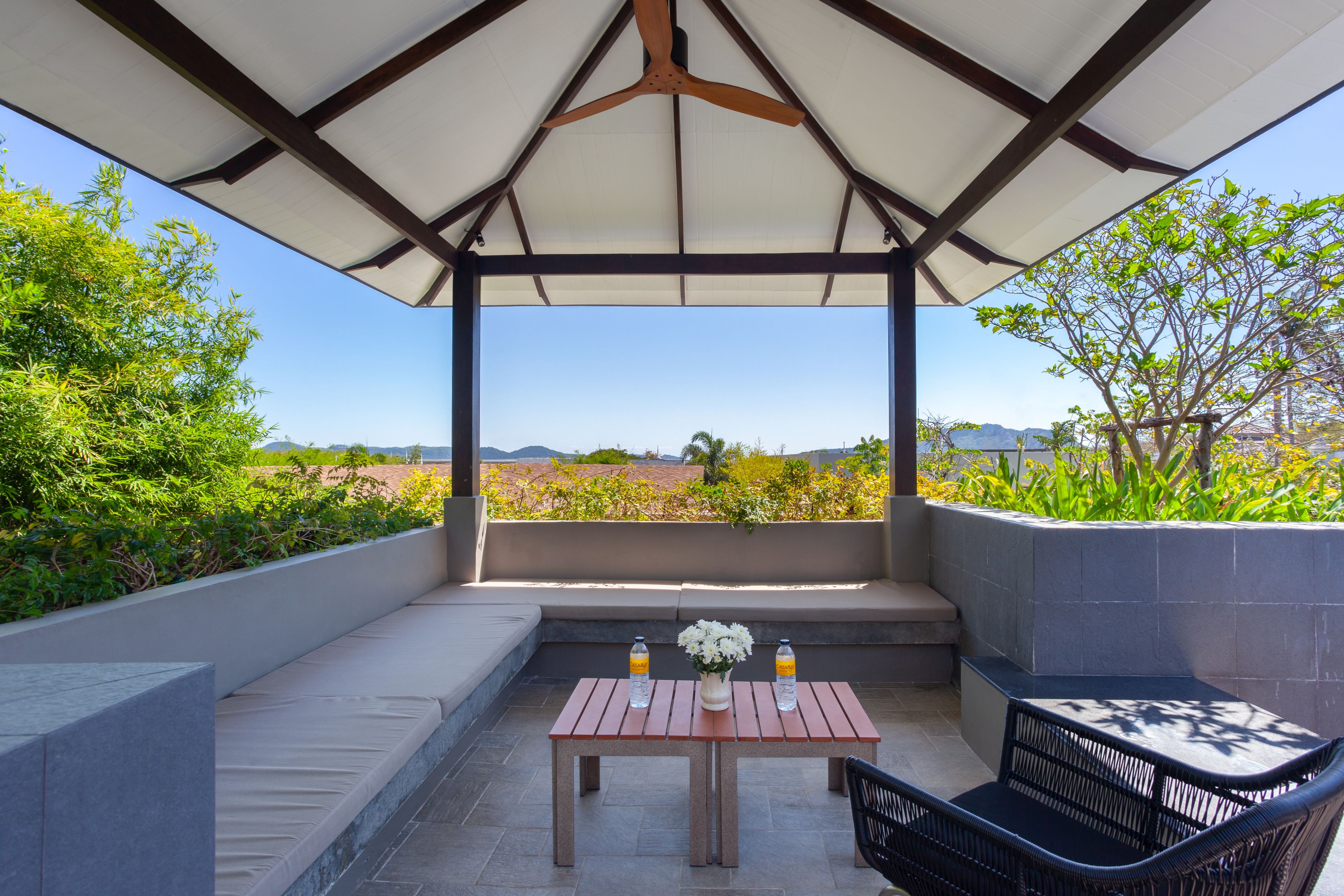 Ein überdachter Außenbereich mit Tisch und Stühlen, Blick auf die Landschaft und Deckenventilator.