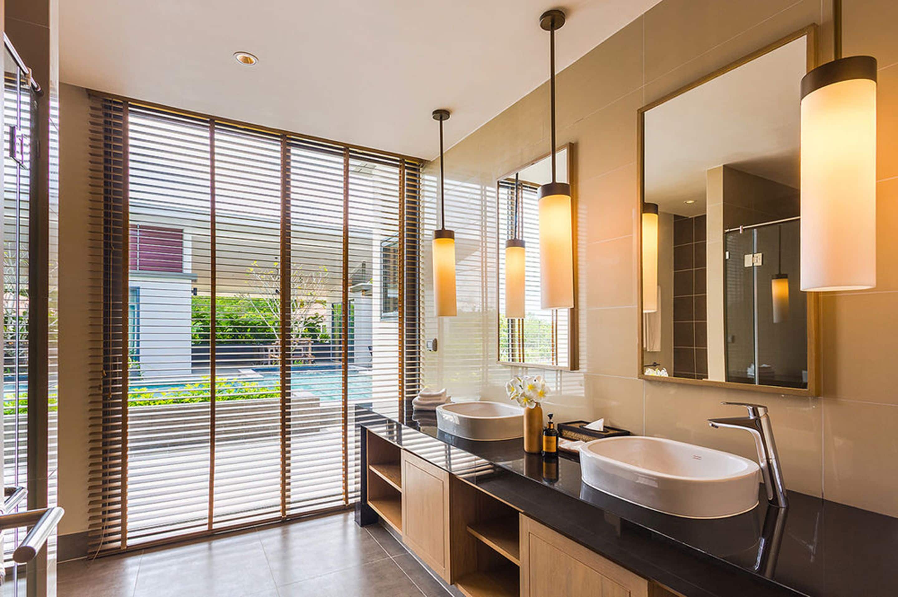 Un baño moderno con dos lavamanos, un espejo grande y vistas a una piscina a través de ventanales de pared a techo.