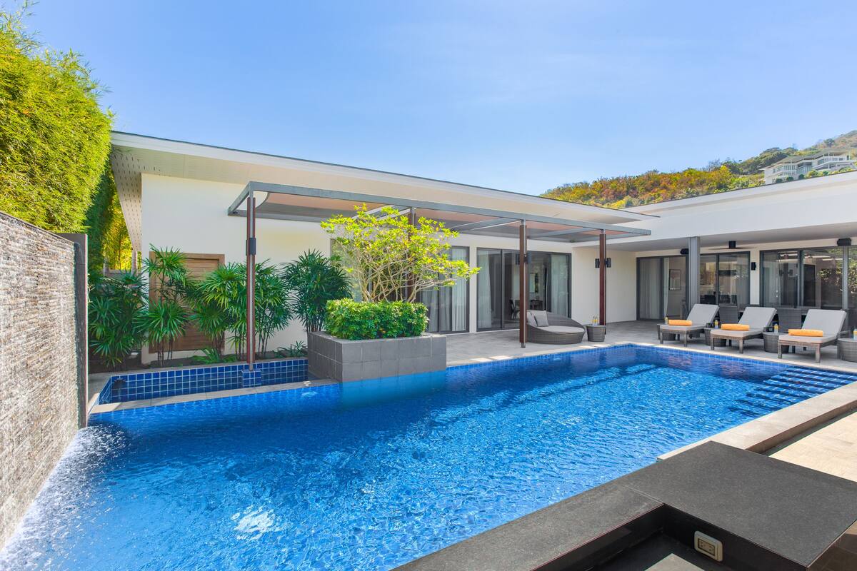 A modern outdoor pool area with a clear blue pool, surrounded by lounge chairs and a covered seating area.