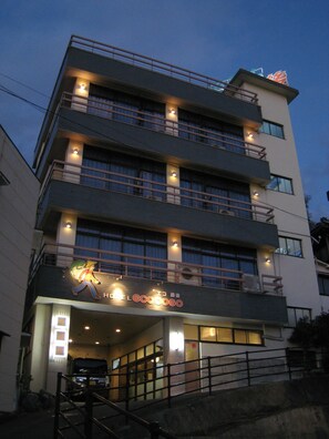 A multi-story hotel with a brightly lit sign featuring a cartoon character. - Eco Dogo - Hostel (Matsuyama)
