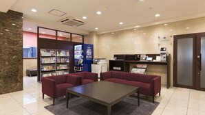 Un hall con mostrador de recepción, máquina de café y zona de estar con dos sofás y una mesa.