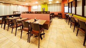 Un restaurante con varias mesas y cabinas, una barra con carta y suelo de baldosas.