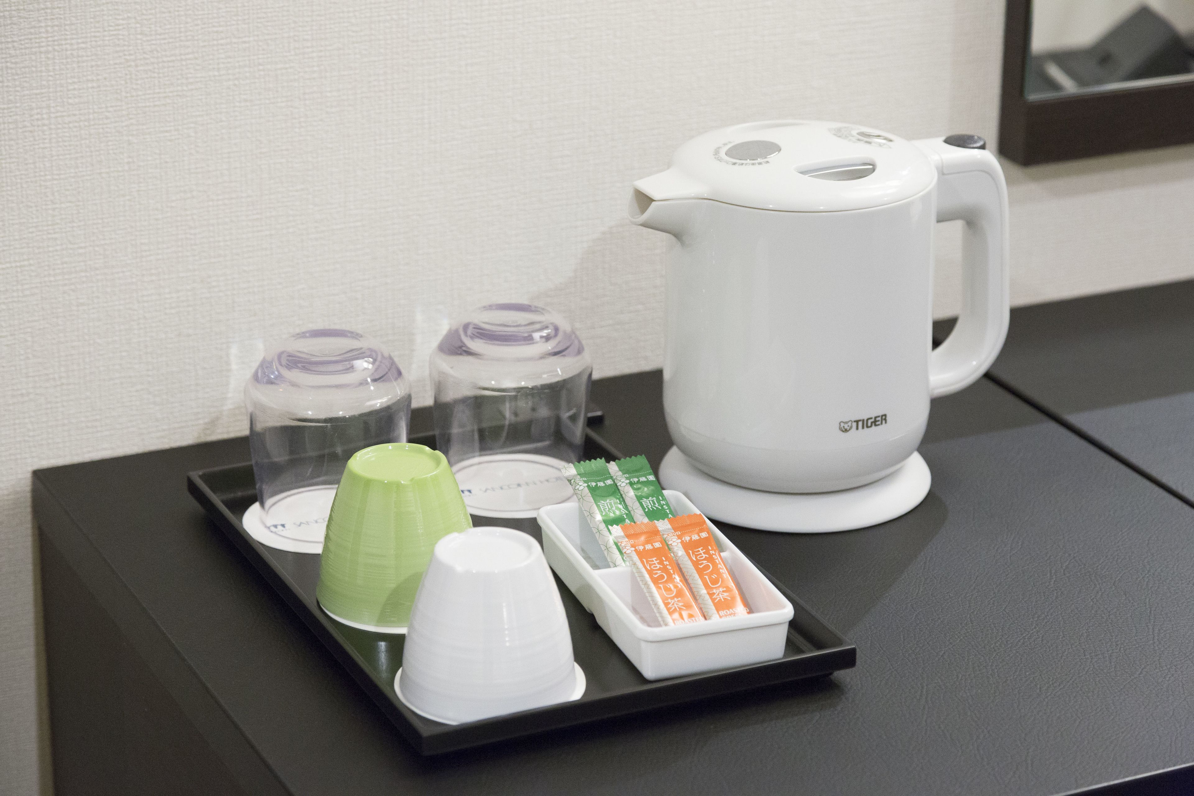 A tray with a white mug, green and white cups, and sachets on a black tray.