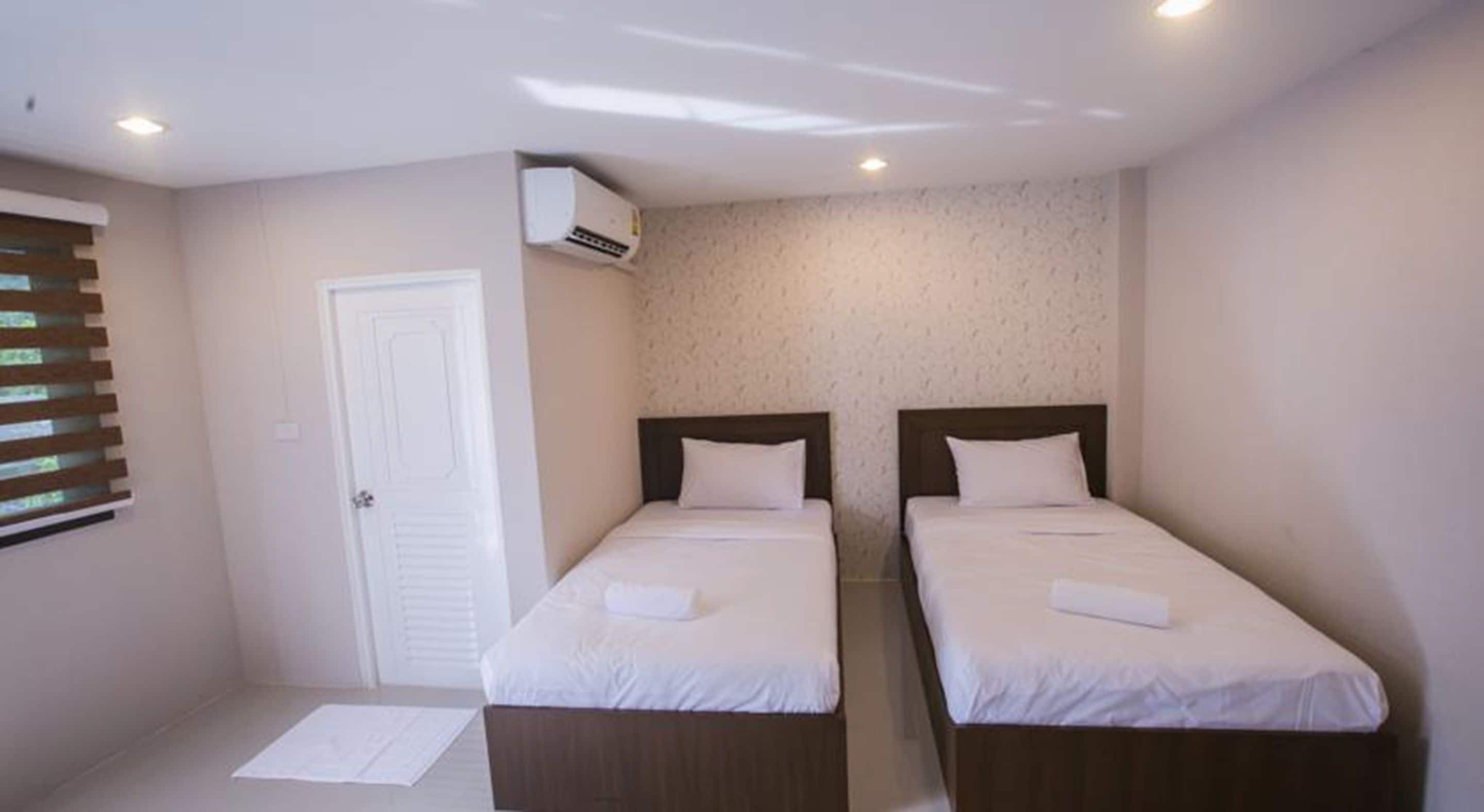 A small, clean room with two single beds, a white door, and an air conditioning unit on the wall.