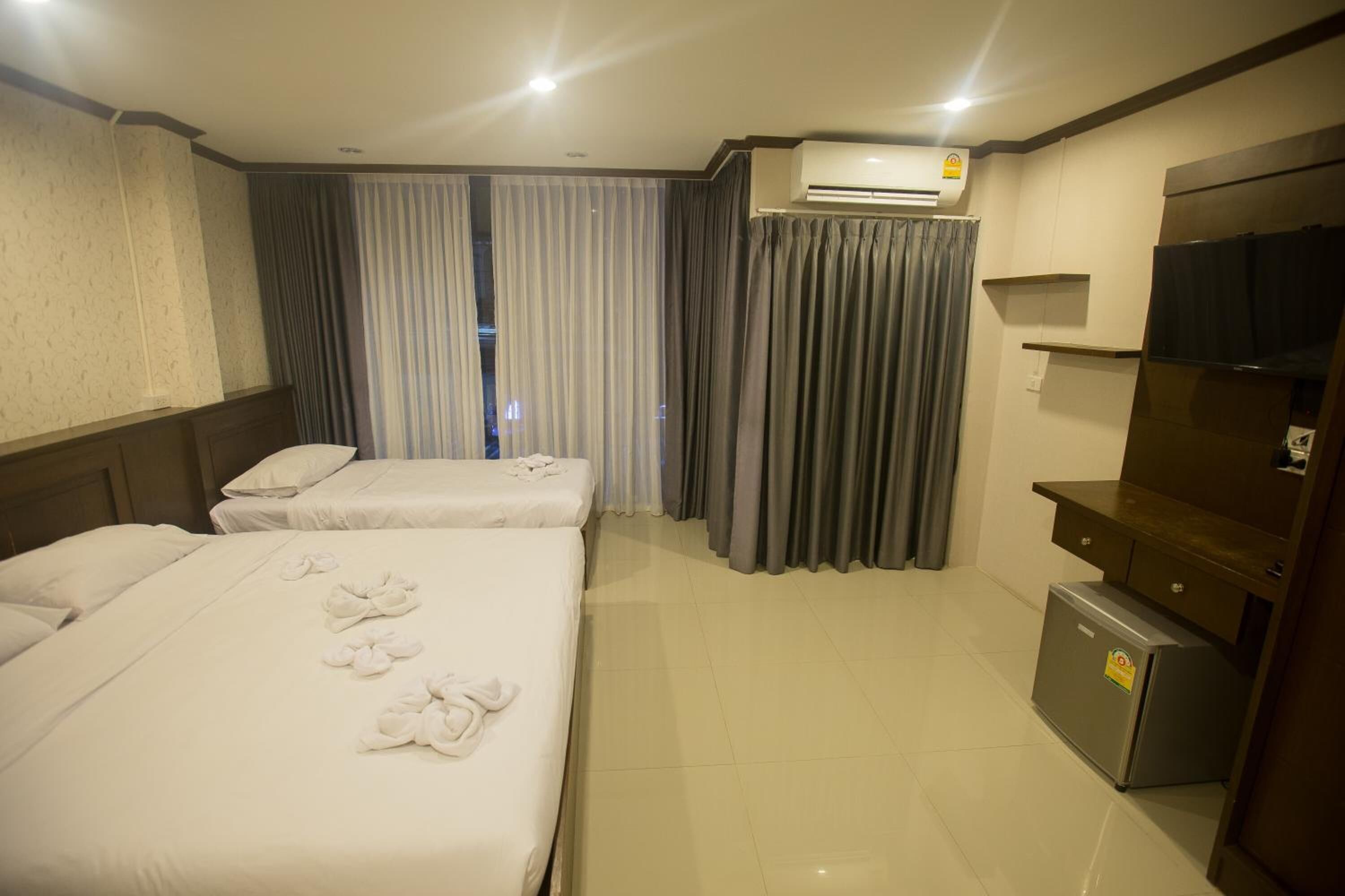 A hotel room with two beds, a small refrigerator, an air conditioning unit, and a television.