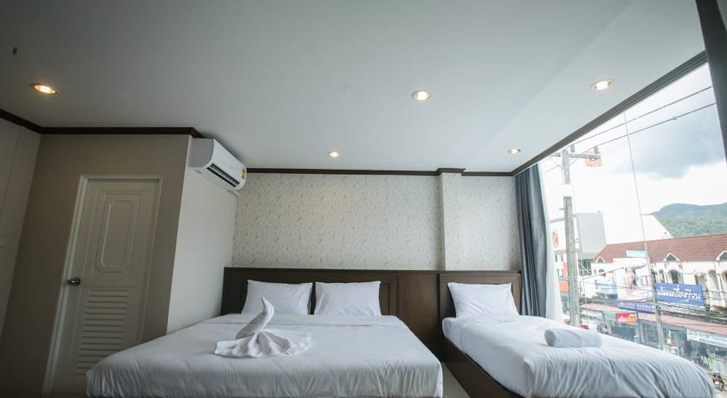 A hotel room with two beds, an air conditioning unit, a large window with a view of the city, and a door.