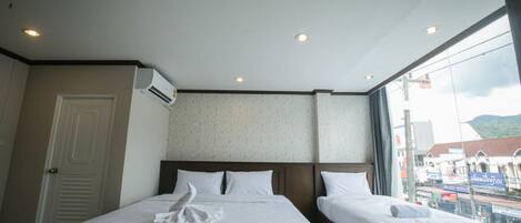 A hotel room with two beds, an air conditioning unit, a large window with a view of the city, and a door.