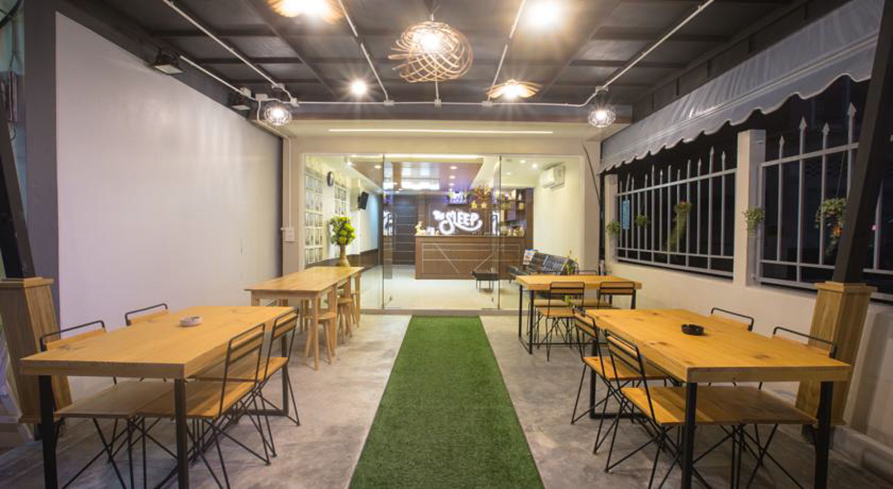 A modern office space with multiple wooden tables and chairs, a green carpet, and a reception area with a sign reading "The Sleep".