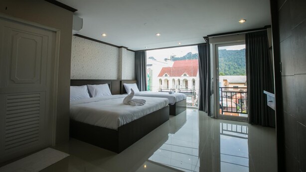 Una habitación de hotel moderna con una cama grande, un balcón con vistas a edificios y colinas, y un espacio bien iluminado.