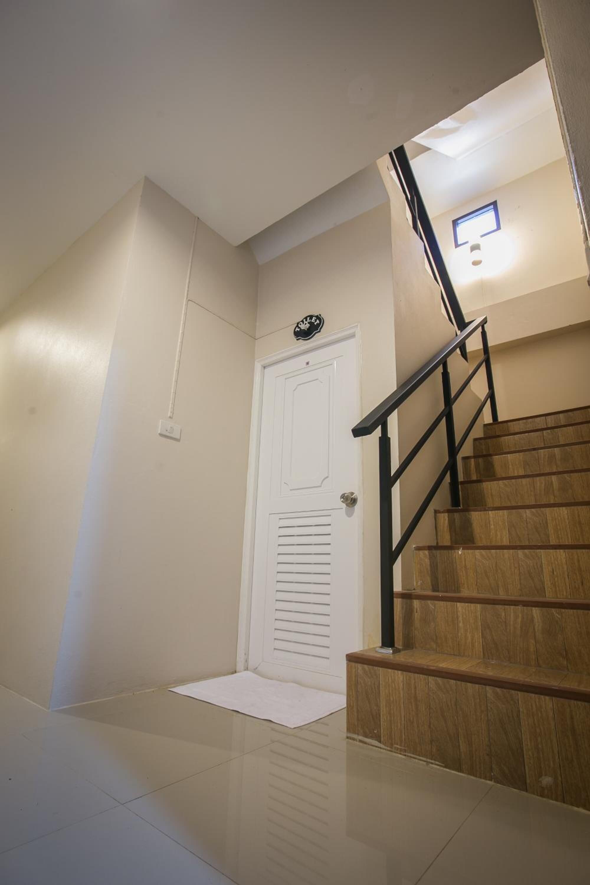 Una escalera de madera con barandilla negra que lleva a una puerta blanca con un pequeño ventanal en la parte superior.