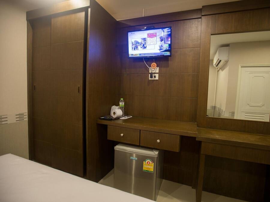 A hotel room with a wooden wardrobe, a small refrigerator, a flat-screen TV mounted on the wall, and a mirror above the counter.