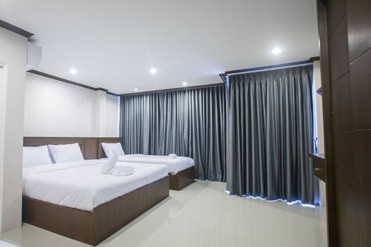 Una habitación de hotel con una cama grande, dos mesitas de noche, un armario y una ventana con cortinas.