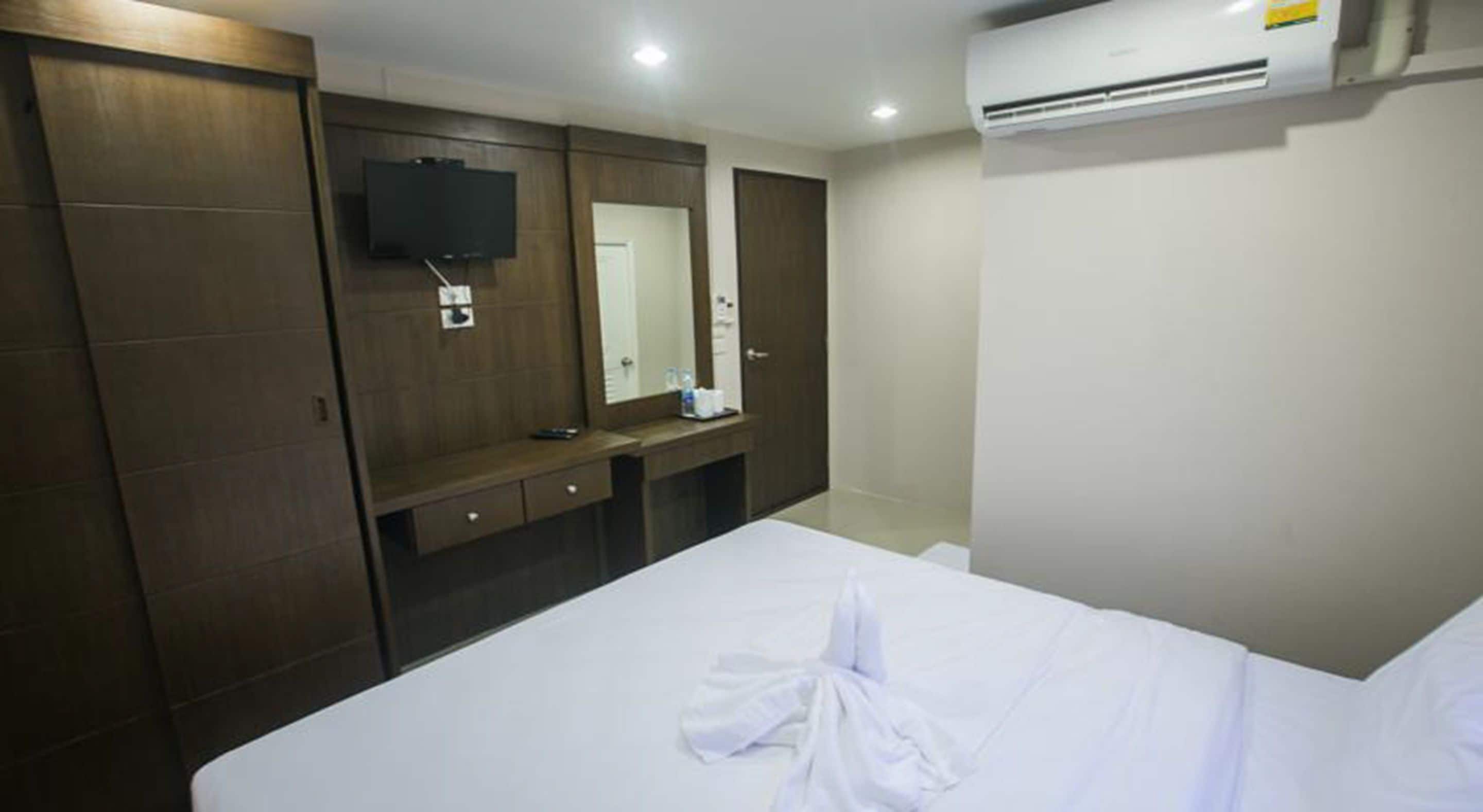 Habitación de hotel con una cama grande, un armario de madera, un televisor de pantalla plana montado en la pared y un equipo de aire acondicionado.