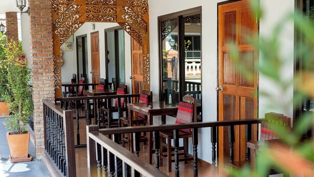 A traditional wooden balcony with a railing, potted plants, and a view of the street. - Gita's House (Chiang Rai)