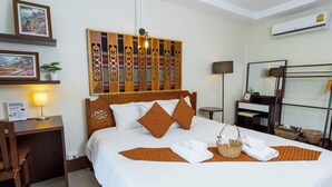 A neatly made bed with a patterned bedspread, two pillows, a bedside lamp, and a wall-mounted decorative panel. - Gita's House (Chiang Rai)
