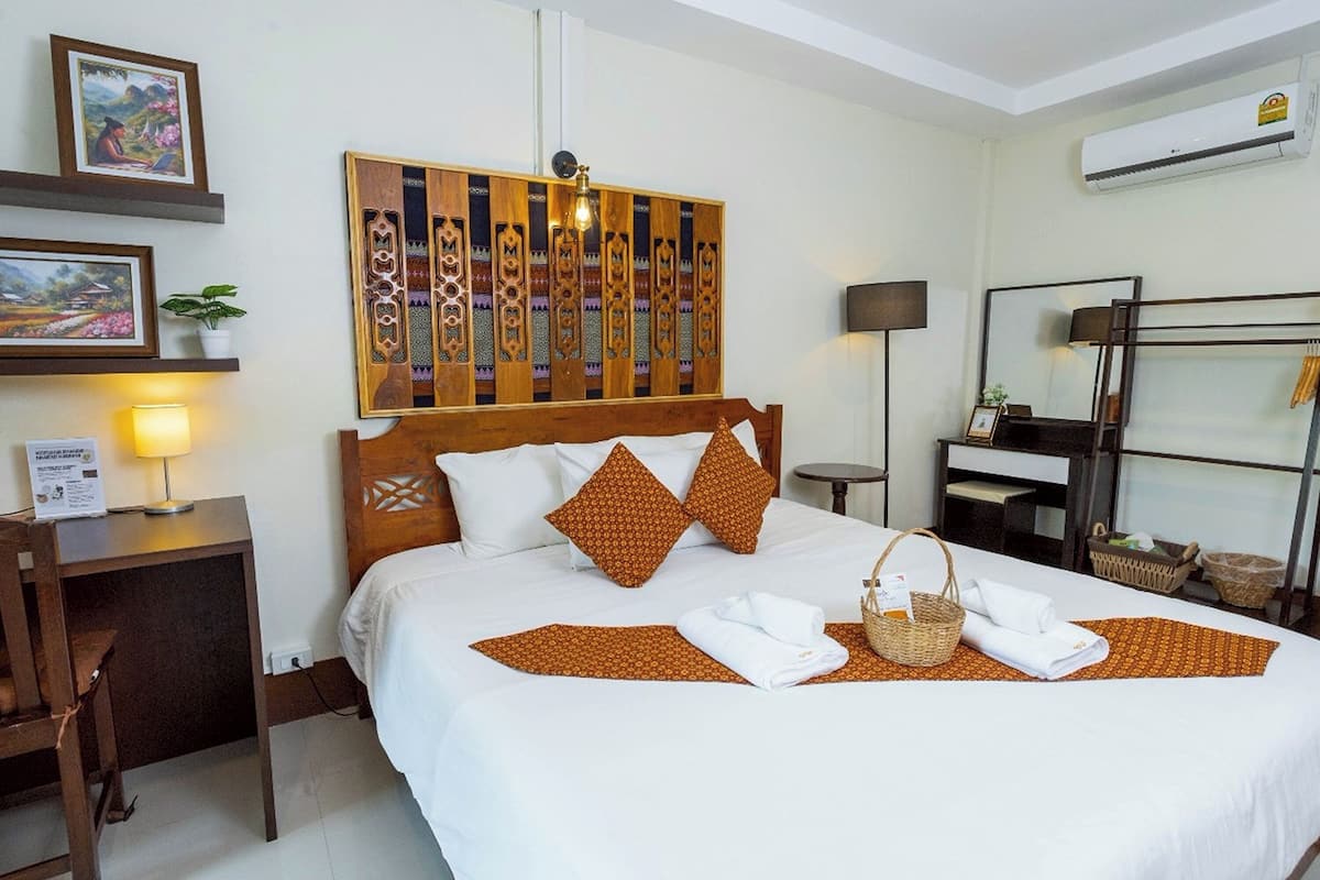 Una cama bien tendida con una colcha estampada, dos almohadas, una lámpara de noche y un panel decorativo en la pared.