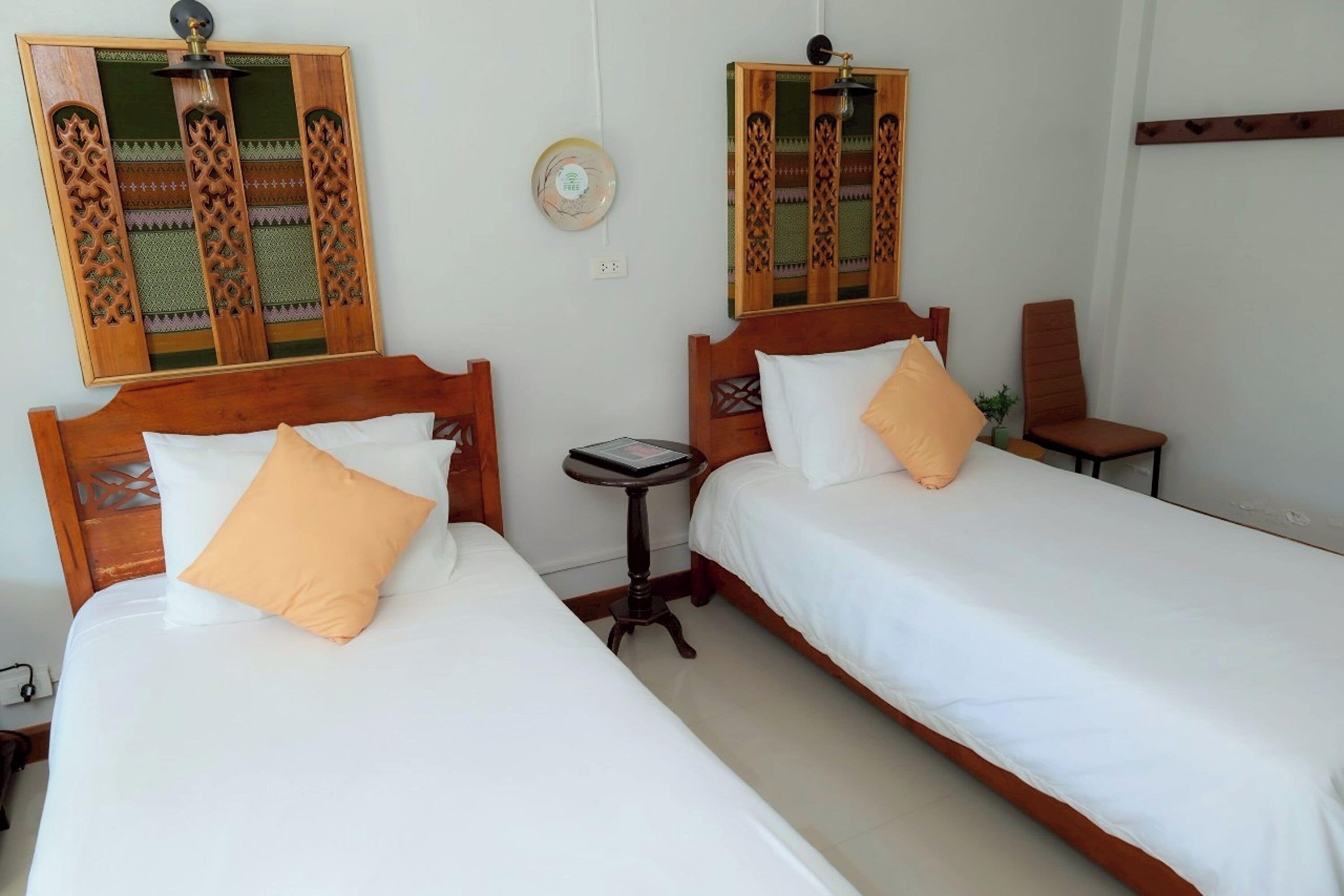 Two single beds with wooden headboards, white bedding, and orange pillows. There is a small round table between the beds.