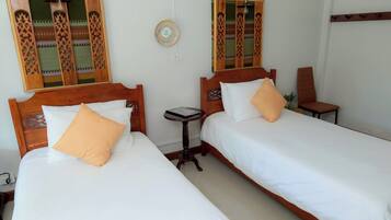Two single beds with wooden headboards, white bedding, and orange pillows. There is a small round table between the beds.