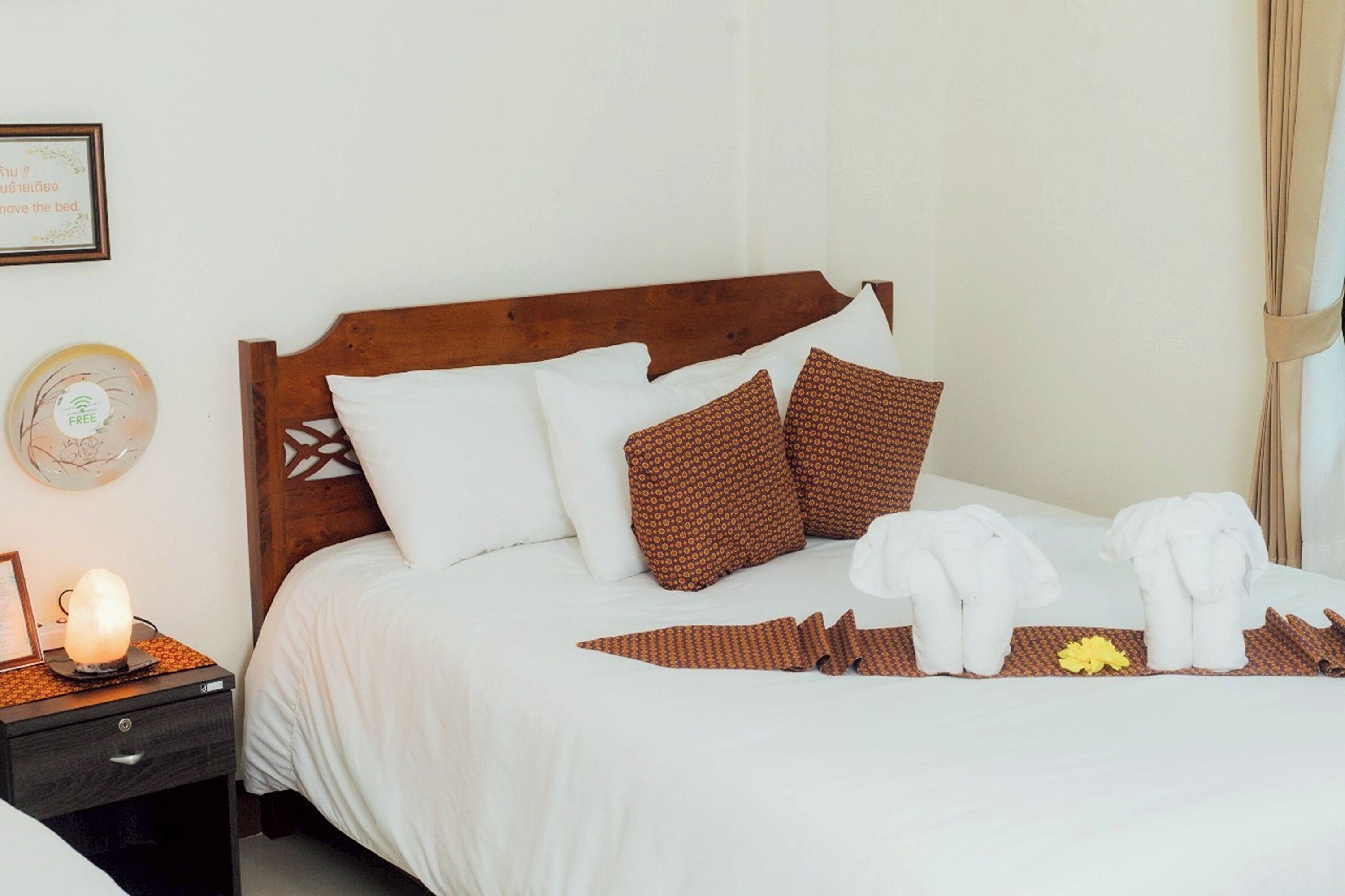 A neatly made bed with white linens and brown patterned pillows, a bedside table with a lamp, and a framed certificate on the wall.