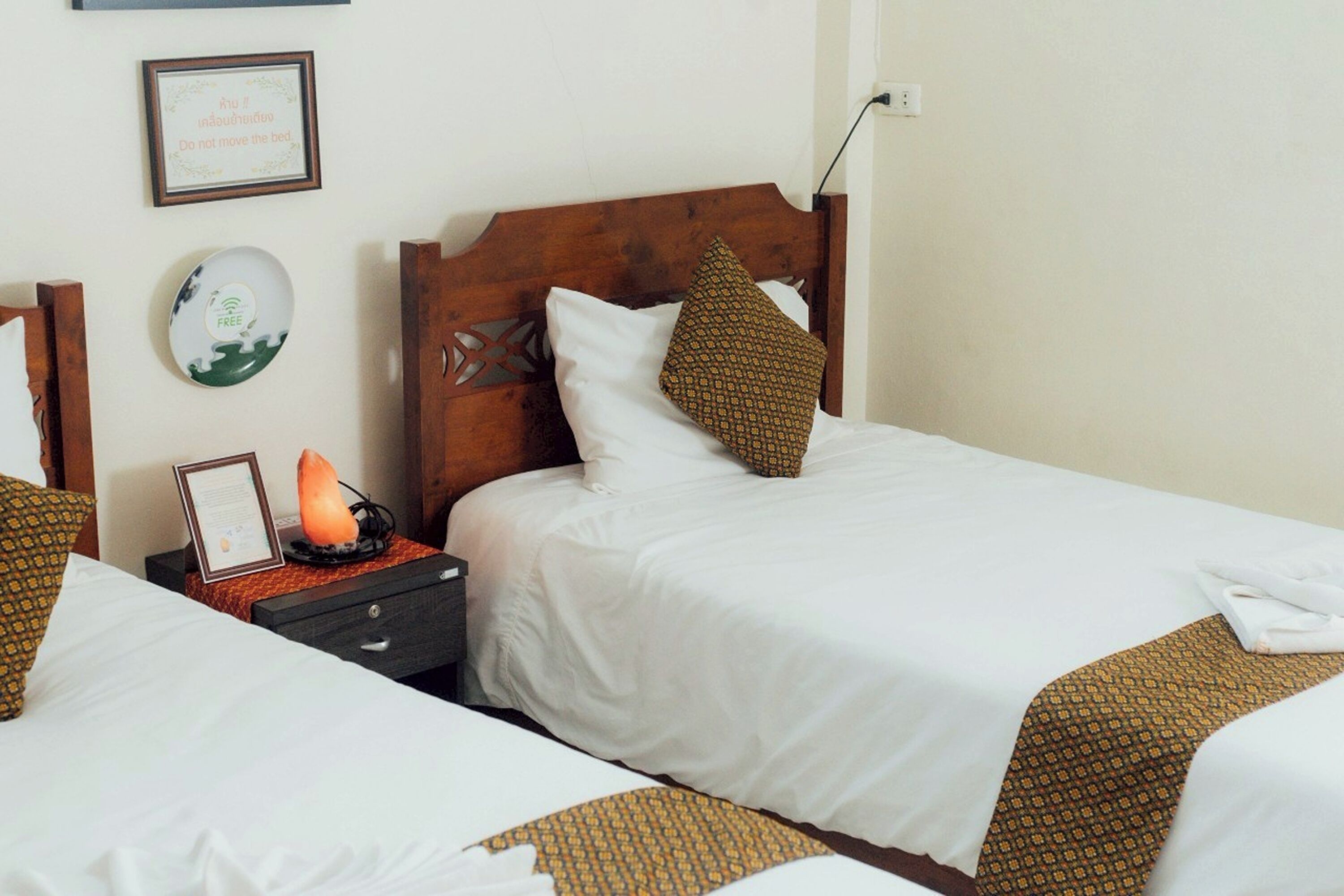 A hotel room with two beds, a nightstand with a lamp, a framed sign, and a wall-mounted plate.