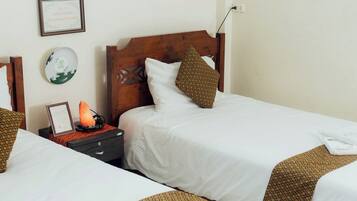 A hotel room with two beds, a nightstand with a lamp, a framed sign, and a wall-mounted plate.