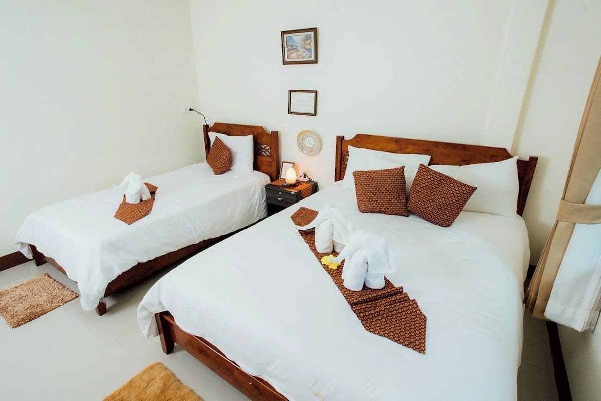 Dos camas individuales con cabeceros de madera, ropa de cama blanca y almohadillas decorativas marrones. Cada cama tiene una mesita de noche con lámpara.