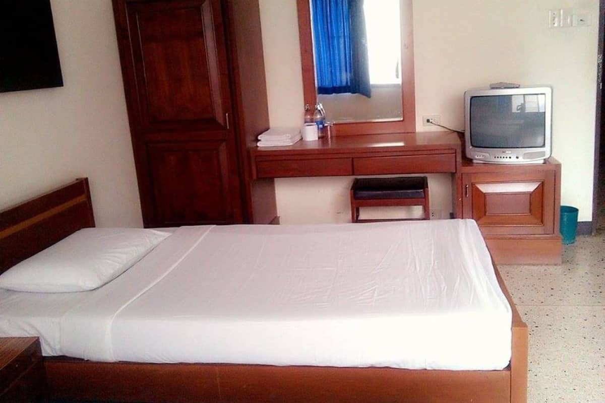 A room with a bed, a wooden desk, a television, and a window with a curtain.