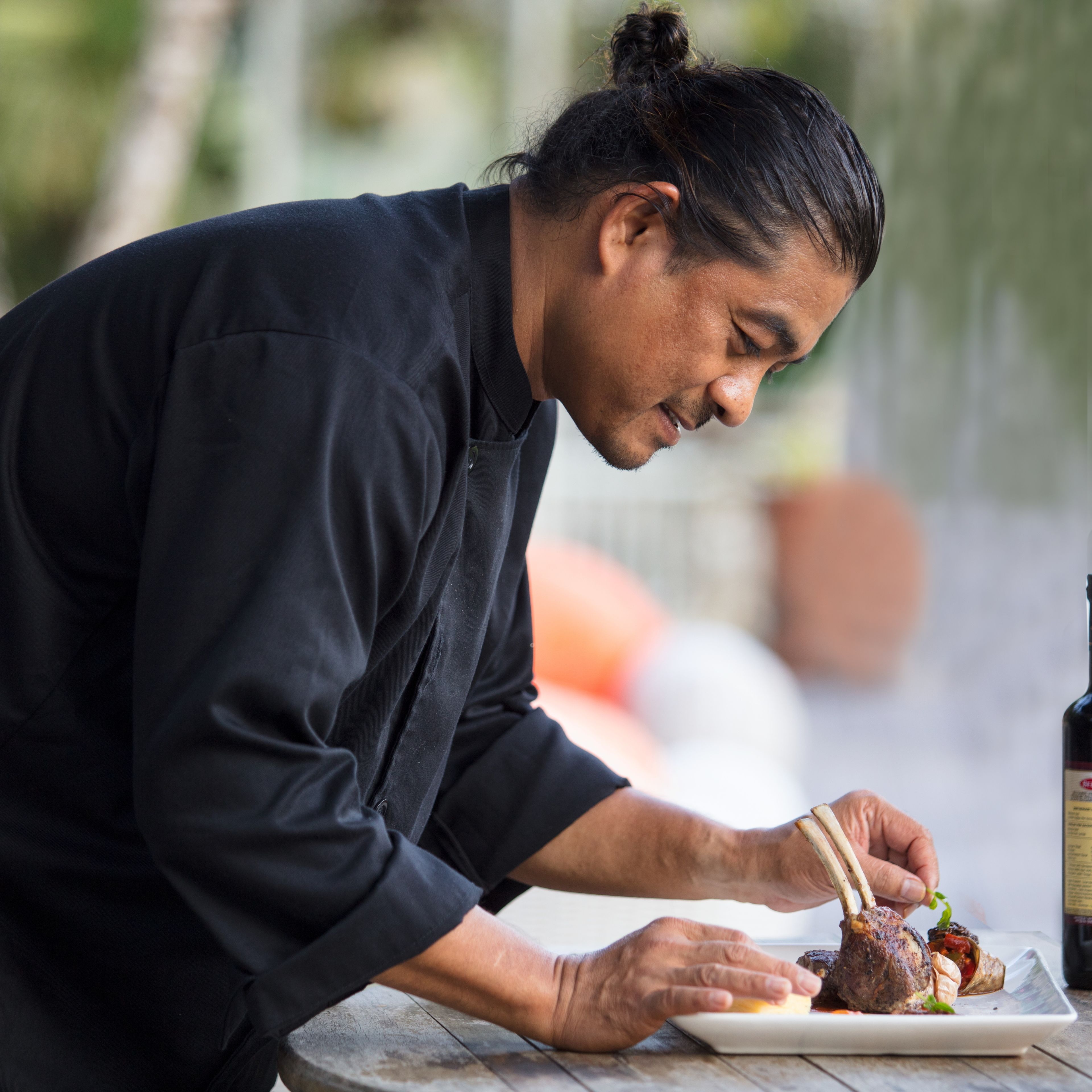 A person in a black chef's coat preparing food on a white plate.