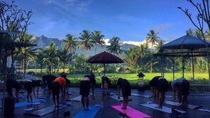 A group of people on yoga mats outdoors with a scenic view of palm trees and mountains in the background. - Plataran Heritage Borobudur Hotel (Borobudur)