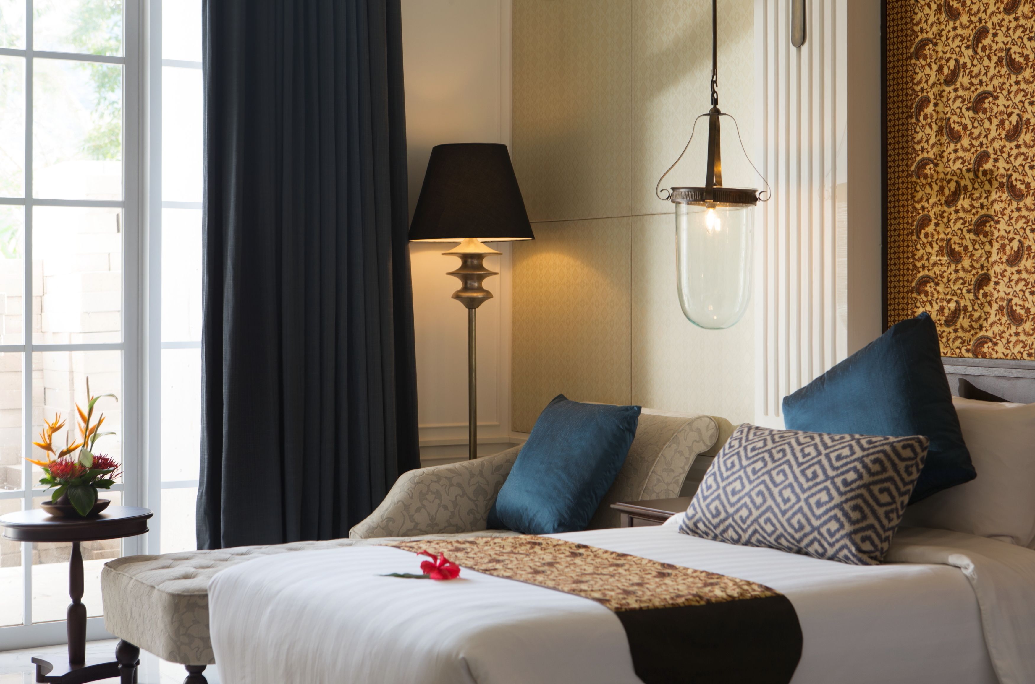 A neatly arranged hotel room with a bed, a bedside lamp, and a view through a window.