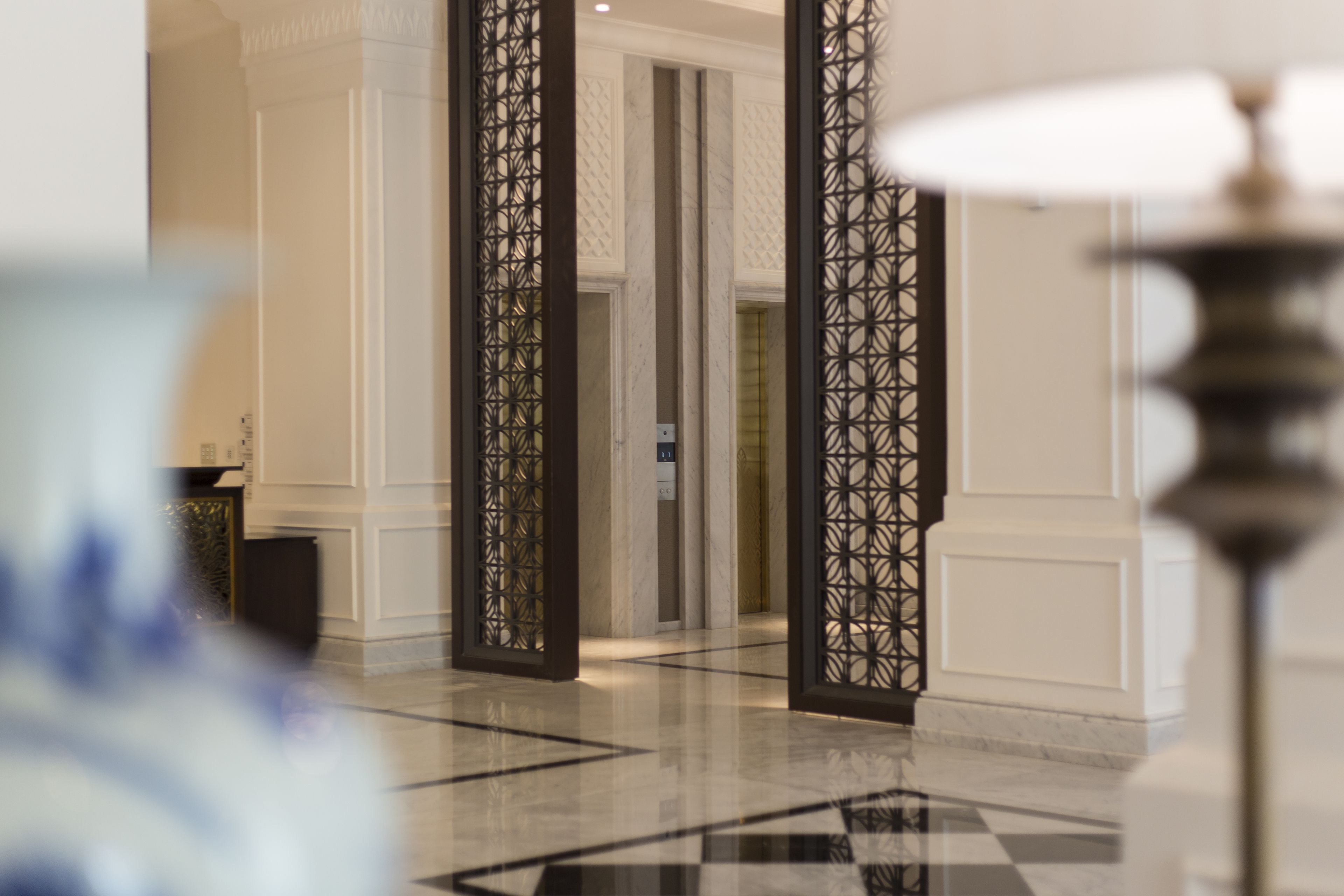 A corridor with a checkered floor, a decorative black partition, and a white wall with a textured pattern.