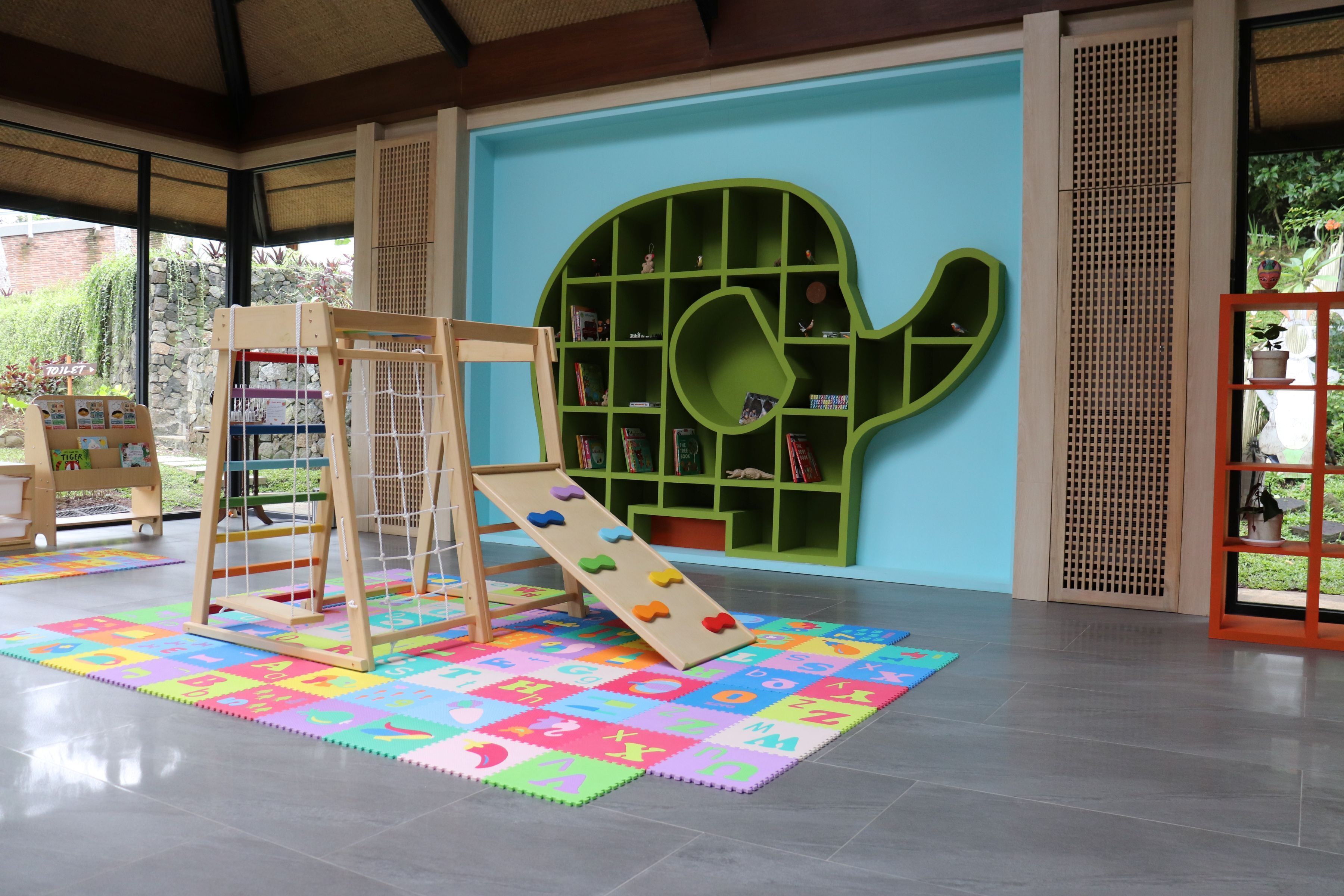 Zona de juegos con un tobogán de madera, una escalera de escalada y una estantería verde.