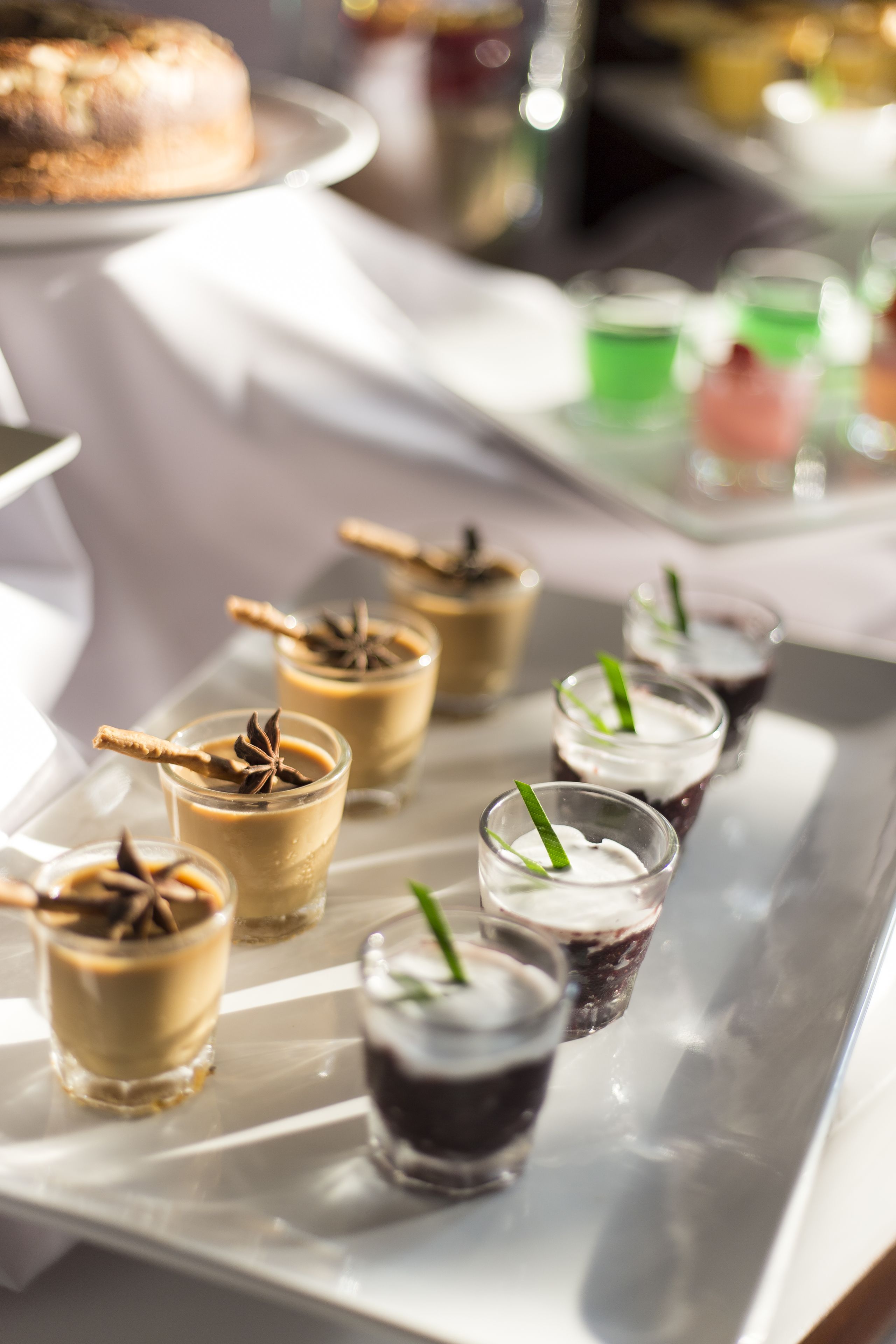 Una bandeja con diversos postres, como pasteles en capas y vasos pequeños con bebidas, probablemente para un bufé o evento.